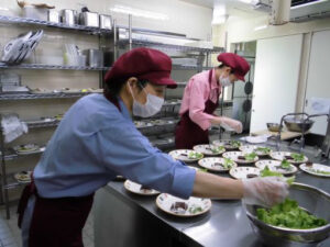 介護施設の厨房で食事準備をするスタッフ。複数の調理員が協力して配膳に取り組む。